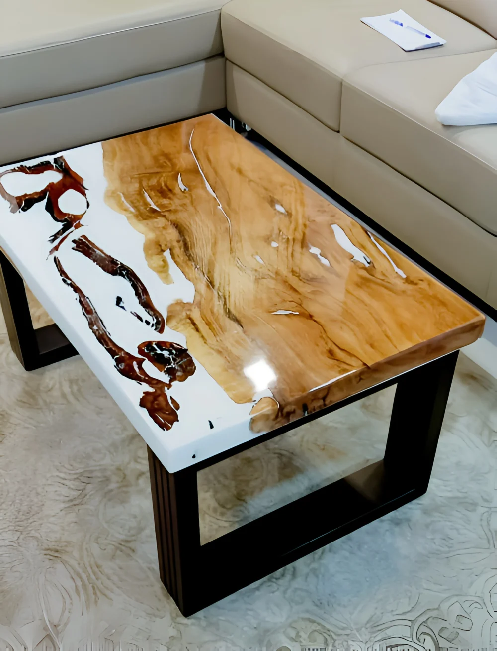 A modern coffee table with a polished, resin-filled wood top and a black metal frame sits in front of a beige leather sectional sofa