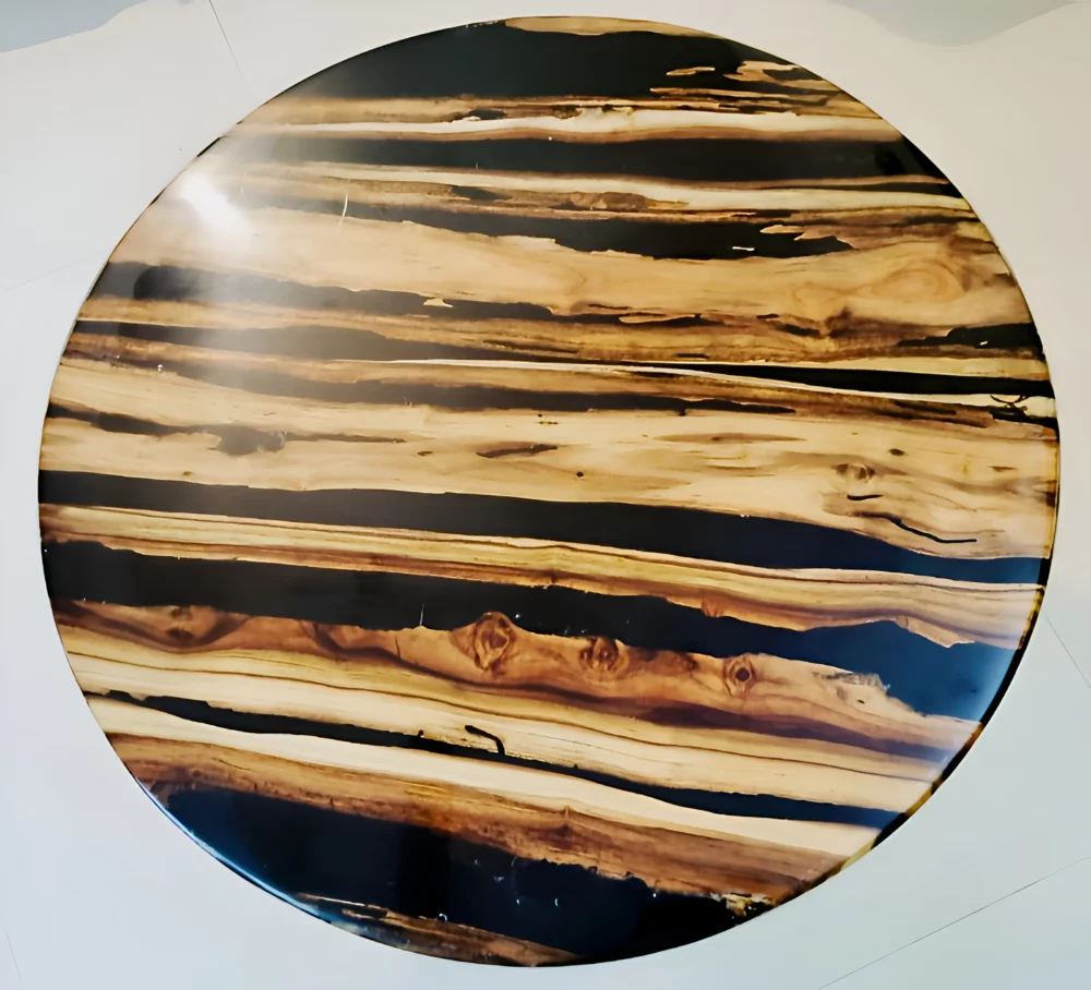 A round tabletop made of wood slabs interspersed with black resin, creating a striking visual pattern.